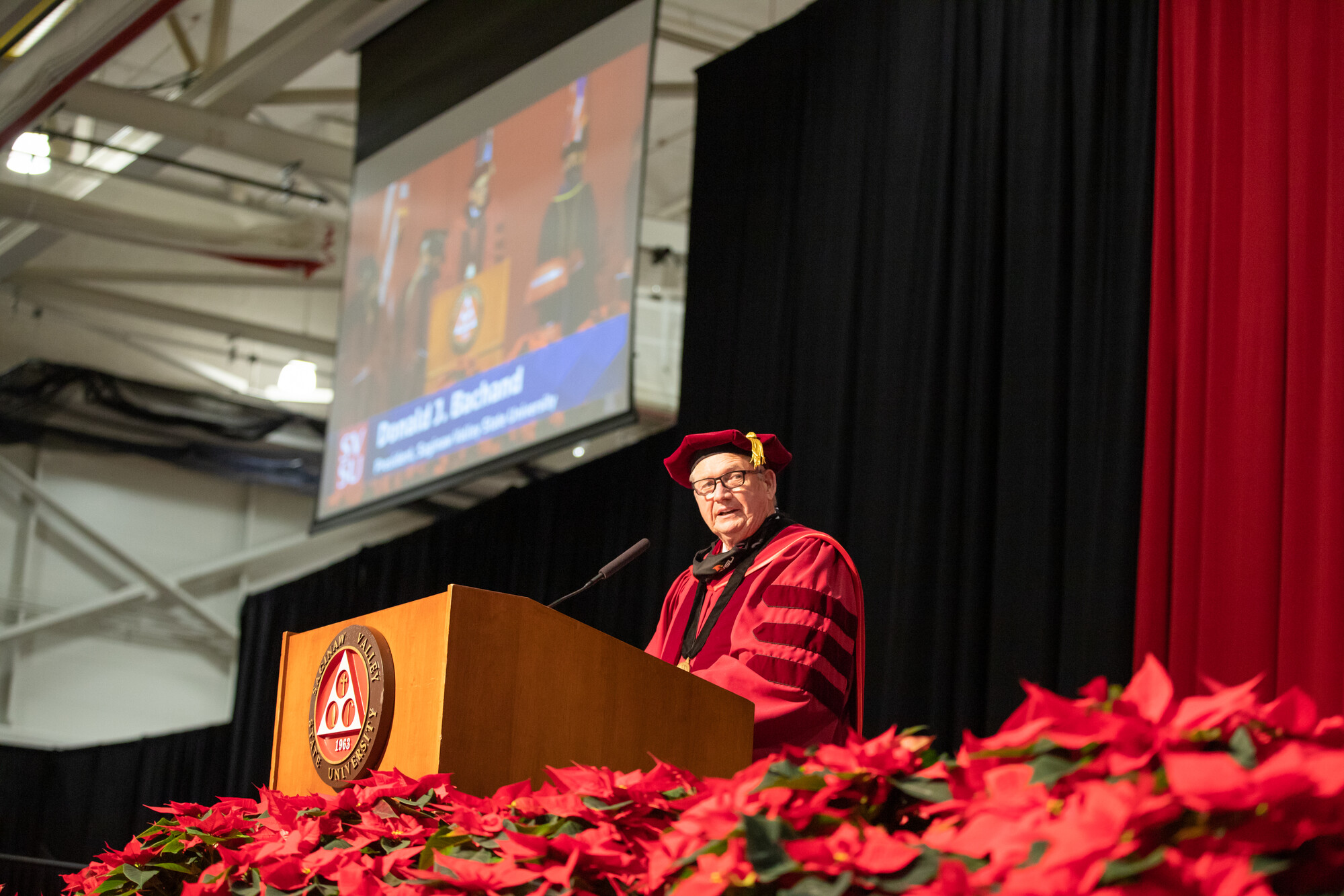 man at lectern, pointsettias in foreground